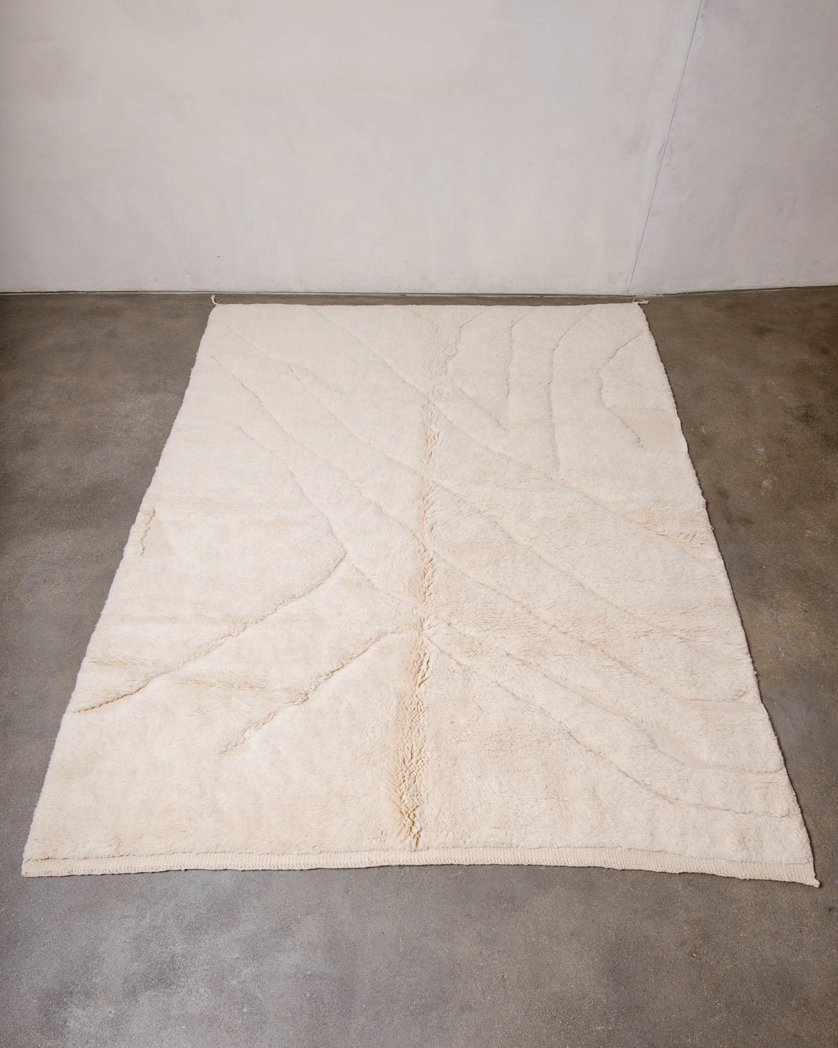 Beni M'rirt rug in cream wool with abstract woven line design, laying flat on concrete studio floor.